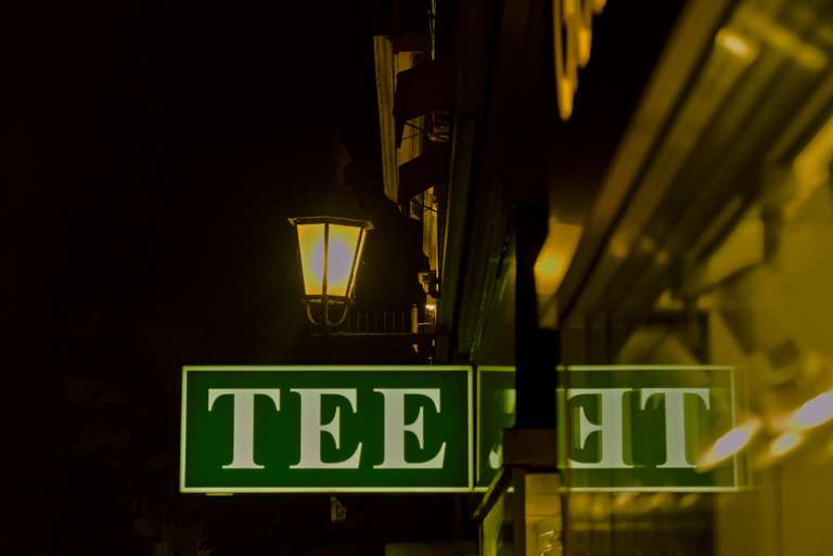 A TEE sign on the side of a building at night, with a street lamp lit above it