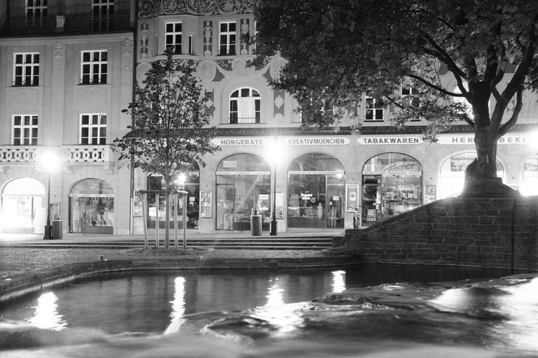 A fountain, a tree, and a building in the background, shot at night