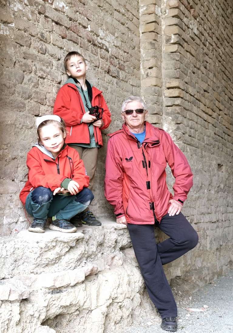 Three people, two boys and a man, in red jackets posing against a faded brick wall