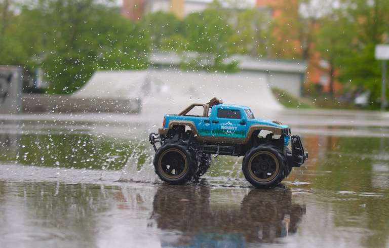 An RC car racing across a puddle, with water droplets captured still around them