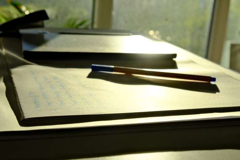 A pen on a paper block backlit by the morning sun
